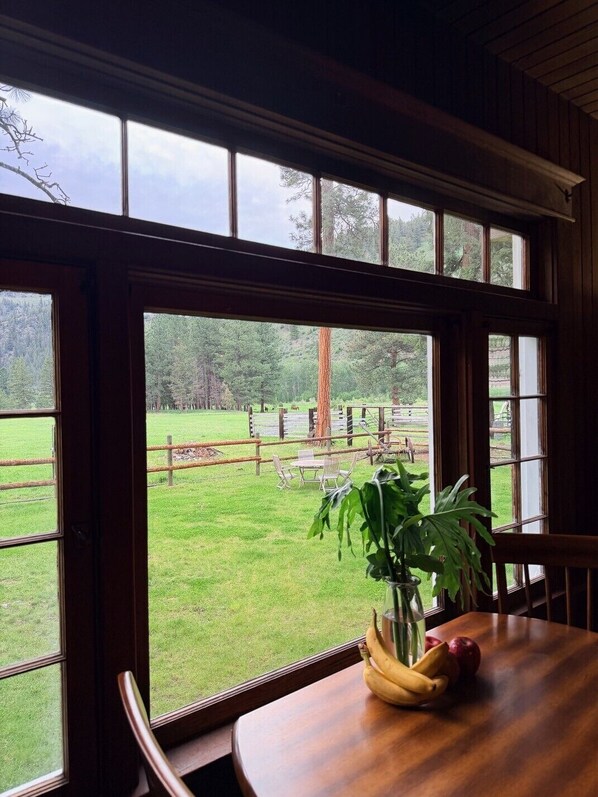 A room with a large window overlooking a grassy area with trees and a fence.