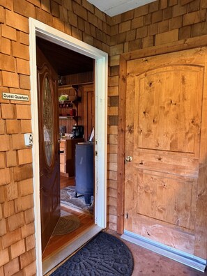 A wooden door with a sign reading 'Guest Quarters,' a black mat at the entrance, and a glimpse of a kitchen area with a coffee maker.