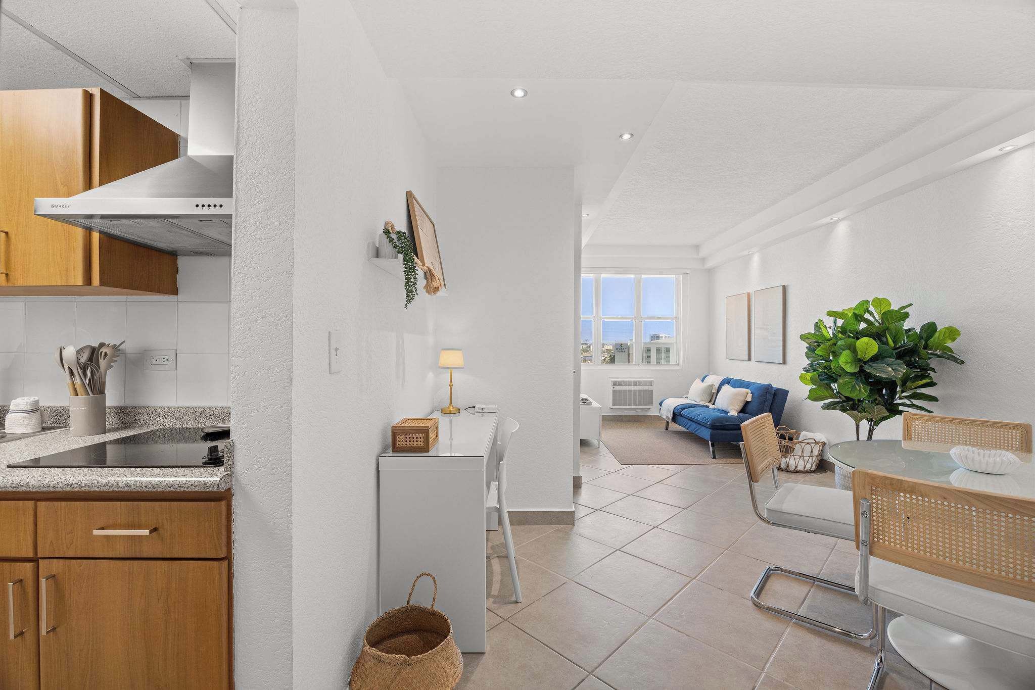 Une cuisine moderne dotée d’une cuisinière intégrée, de meubles blancs et d’un coin repas avec une table en verre et des chaises en osier.