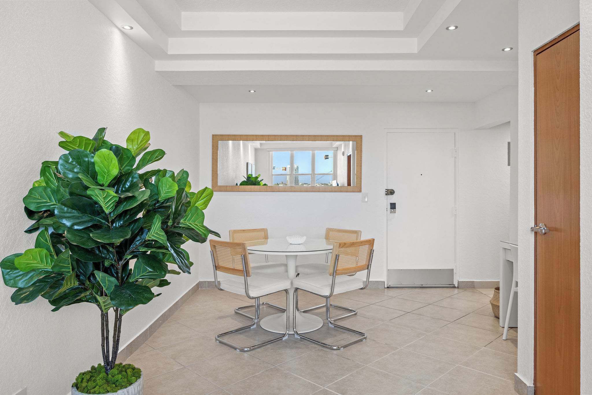 Un espace repas moderne avec une table ronde, quatre chaises et une grande plante en pot.