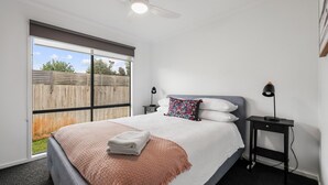 Een slaapkamer met een bed, nachtkastje, lamp, plafondventilator en uitzicht op de omgeving.