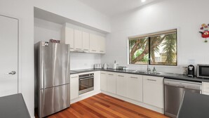Een moderne keuken met roestvrijstalen apparatuur, witte kasten en een groot raam met uitzicht op bomen.