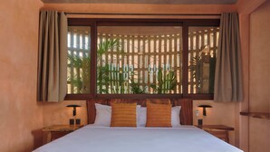 A hotel room with a bed, two bedside tables, a nightstand, a window with curtains, and a view of palm trees. - Casa Tintorera (Santa María Colotepec)