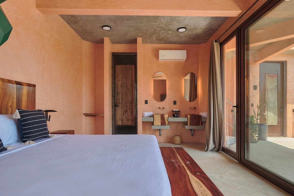 A bedroom with a large bed, a wooden headboard, a bathroom with a sink and mirror, and a sliding glass door to the outside.
