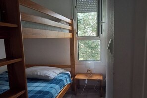 Ein Etagenbett mit blauer Karomattreze, ein Nachttisch mit Lampe und ein Fenster mit Rollo.