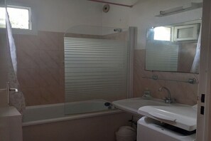 A bathroom with a bathtub, a sink, a mirror, and a window. - Apartment 50 metres from sandy beach overlooking wooded garden (Mauguio)