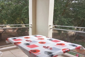 Ein Balkon mit Tisch, bedeckt mit einer blumigen Tischdecke, umgeben von Bäumen.
