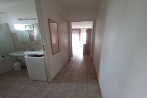 Ein schmaler Flur mit einem Badezimmer auf der linken Seite, ausgestattet mit einem Waschbecken und Spiegel.