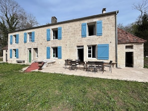 A two-story stone building with blue shutters, a patio with outdoor furniture, and a small garden area.
