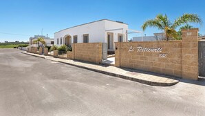Un edificio moderno con facciata bianca, un muro in pietra con la scritta 'Peticurti B&B' e una palma davanti.