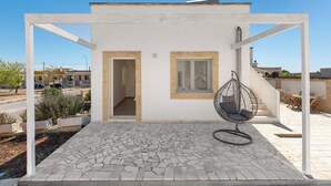 Un edificio bianco con un patio, una sedia a dondolo e vista sulla strada.