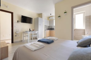 Ein Hotelzimmer mit Bett, Schreibtisch, Stuhl, Fernseher, Küchenzeile und Bad.