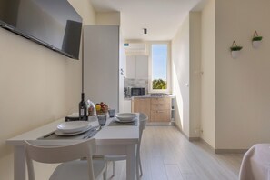 Eine moderne Küche mit weißen Schränken, einem an der Wand befestigten Flachbildfernseher und einem Essbereich mit weißen Stühlen und einem Tisch für zwei Personen.