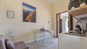A modern kitchen with a sink and stove, a dining area with a table and chairs, a sofa, and a painting on the wall. - Ulivo di Rocco - Bilo Standard PT by BarbarHouse (Cannole)