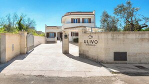 Ein verschlossenes Tor zu einem Anwesen namens 'ULIVO DI ROCCO' mit einem gepflasterten Weg, der zu einem Gebäude mit Ziegeldach führt.