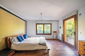 Een slaapkamer met een bed, een kroonluchter, een raam, een radiator en een schuifpui naar een buitenruimte.
