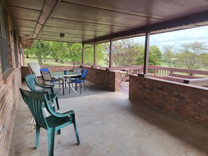 Een overdekt terras met een tafel en stoelen, bakstenen muren en uitzicht op bomen.