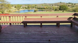 A wooden deck with a bench overlooking a pond and a grassy landscape.