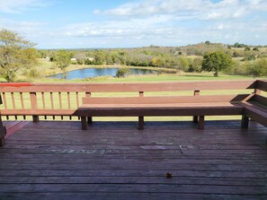 Una terraza de madera con un banco que da a un estanque y un paisaje cubierto de césped.