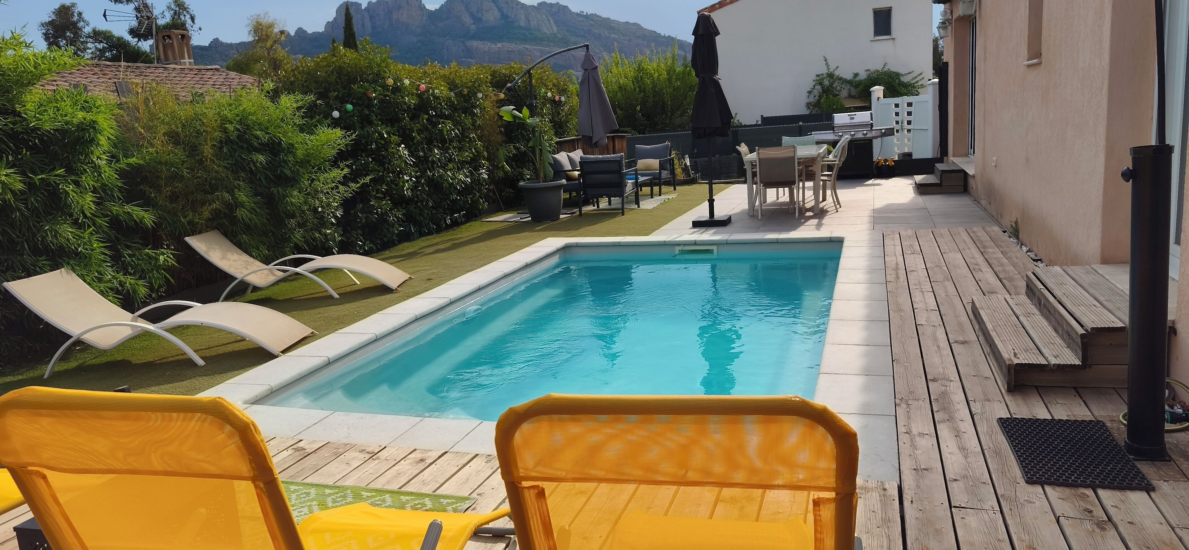 Ein Schwimmbecken mit Liegestühlen, Grillplatz und Blick auf Berge.