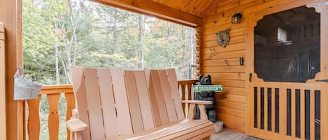 A wooden bench on a porch with a 'Welcome' sign and a Sasquatch statue.