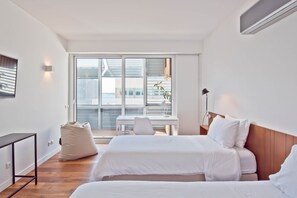 Ein modernes Hotelzimmer mit zwei Betten, einem Schreibtisch, einem Stuhl und einem großen Fenster mit Jalousien.
