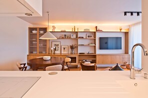 A modern kitchen with a dining table, chairs, a built-in oven, and a large TV mounted on the wall. - Scenic 2 - TERRACE, VIEW & SPACE (Lisbon)
