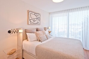 A bedroom with a bed, bedside lamps, a wall-mounted abstract artwork, and a window with sheer curtains. - Scenic 2 - TERRACE, VIEW & SPACE (Lisbon)