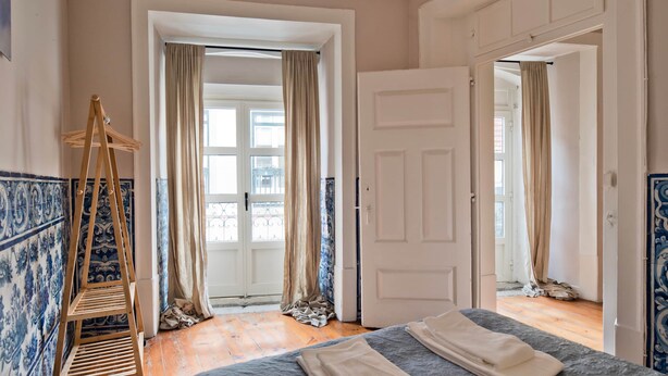 A room with a bed, a wooden hanger, a door, and a view of the outside. - Chiado 5 -  Histórico (Lisbon)