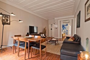 Un soggiorno moderno con un tavolo da pranzo in legno, sedie, un divano in pelle nera, una televisione e una lampada da terra.
