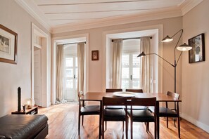 Zona pranzo con tavolo e sedie in legno, una lampada da terra e un letto nell'angolo.