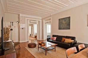 Ein Wohnzimmer mit einem schwarzen Ledersofa, einem Holztisch und einem Fernseher auf einem Holzschrank.