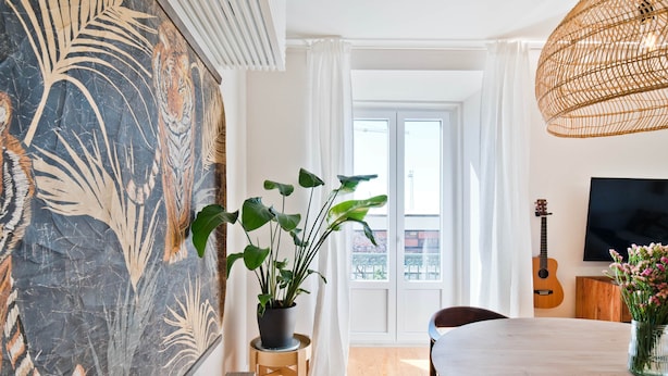 Un área de comedor con una mesa, sillas, una planta en maceta, una guitarra y un televisor en la pared.