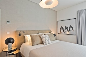 A hotel room with a bed, bedside lamp, wall-mounted light, and a framed artwork. - Ribeira 6 - Boavista Design and Comfort (Lisbon)