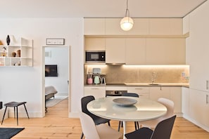A modern kitchen with a glass dining table, white cabinetry, and a microwave. - Ribeira 6 - Boavista Design and Comfort (Lisbon)