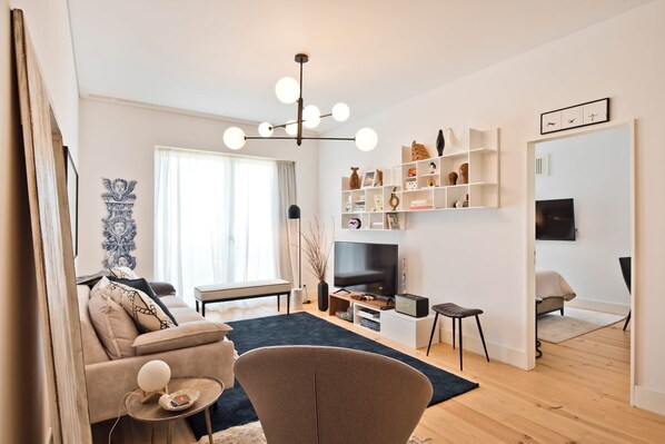 Ein modernes Wohnzimmer mit Sofa, Sesseln, Fernseher und Regalen.