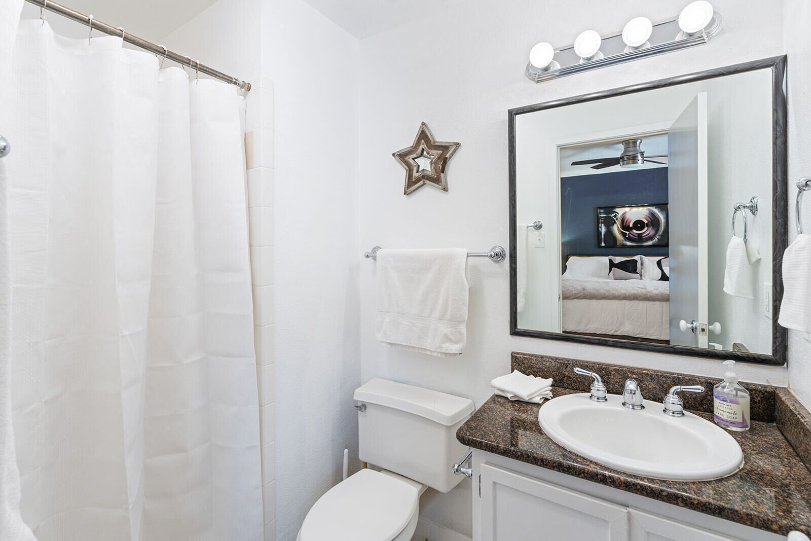 Une salle de bain avec un rideau de douche, des toilettes, un lavabo avec un miroir et une décoration en forme d’étoile sur le mur.