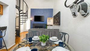 A modern living room with a staircase, a flat-screen TV, a fireplace, and a dining area with a glass table. - Austin Apartments by Andes STR (Austin)