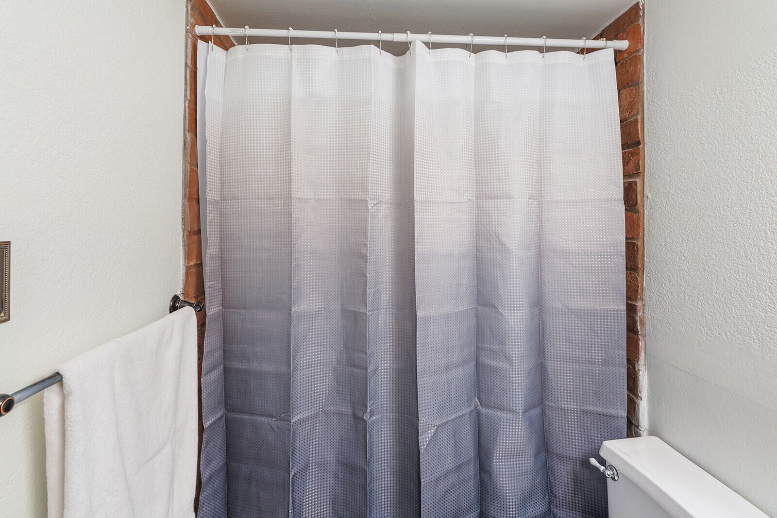 Un baño con cortina de ducha blanca, toallero y retrete.