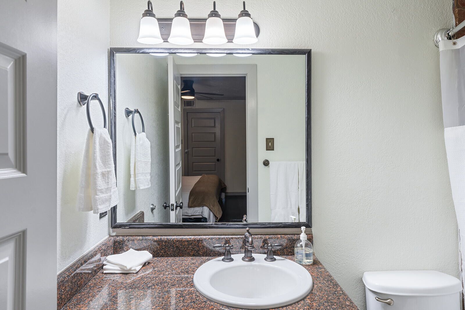 A bathroom with a large mirror, a sink, a toilet, and a towel rack.