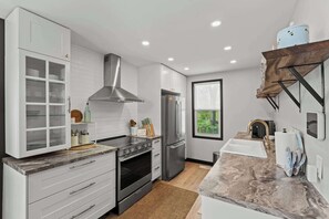 A modern kitchen with white cabinetry, a stainless steel range hood, a built-in oven, and a refrigerator. - The Jade Loft Near Clifton Hill | Soaker Tub 3 Bed (Niagara Falls)