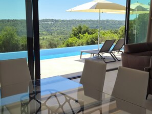 A modern outdoor seating area with a glass table and chairs, a lounge chair, and a large umbrella. - Brand New Luxury Villa Aurea with Infinity Pool & Stunning Views (Čilipi)