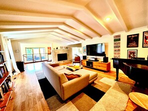 A spacious living room with a large TV, a piano, and a fireplace. - Luxurious, modern 3-br artist’s getaway with downtown views (Tulsa)