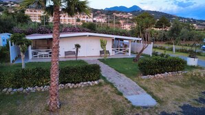 Ein kleines, eingeschossiges Gebäude mit überdachter Terrasse, umgeben von gepflegten Gärten und einem gepflasterten Weg.
