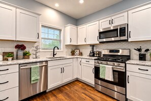 A modern kitchen with stainless steel appliances, white cabinetry, and a wooden floor. - The Locust Estate - Gillham Park - 4 Bedrooms - Walk to KC Streetcar (Kansas City)
