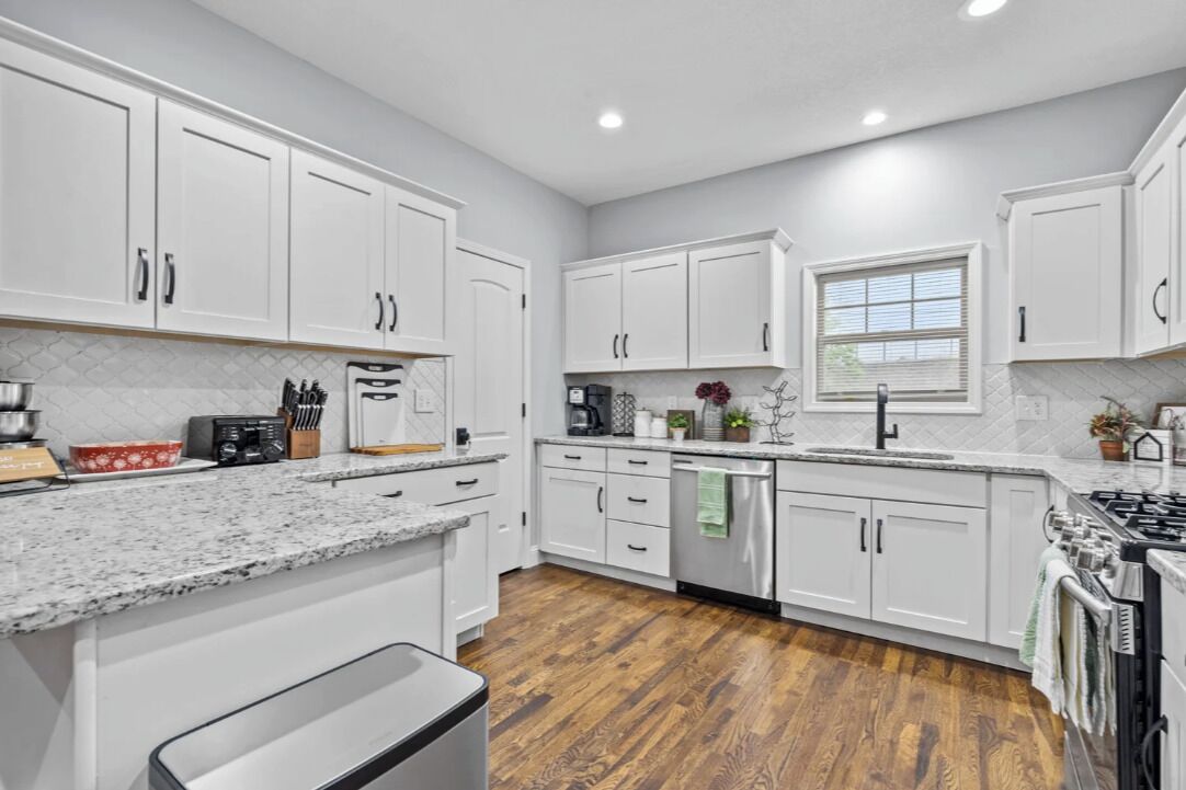 A modern kitchen with white cabinets, granite countertops, a stainless steel dishwasher, and a wood floor.