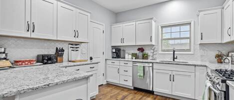A modern kitchen with white cabinets, granite countertops, a stainless steel dishwasher, and a wood floor.