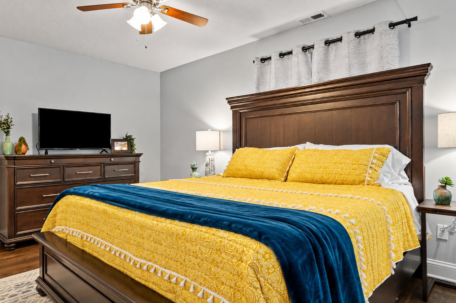 A bedroom with a bed, a television, a dresser, a nightstand, and a ceiling fan.