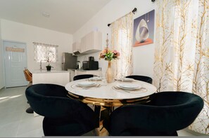 Un comedor con una mesa redonda, sillas negras, un jarrón con flores y una cocina al fondo.