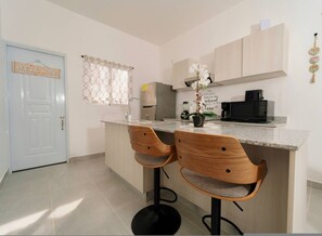 Una cocina moderna con una isla central, dos taburetes de madera, un refrigerador, un microondas y una cafetera.